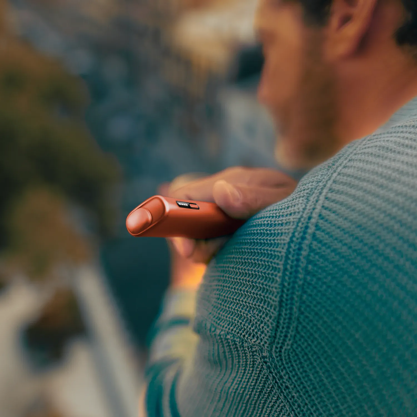 Hands holding a green IQOS device and its charger - green background